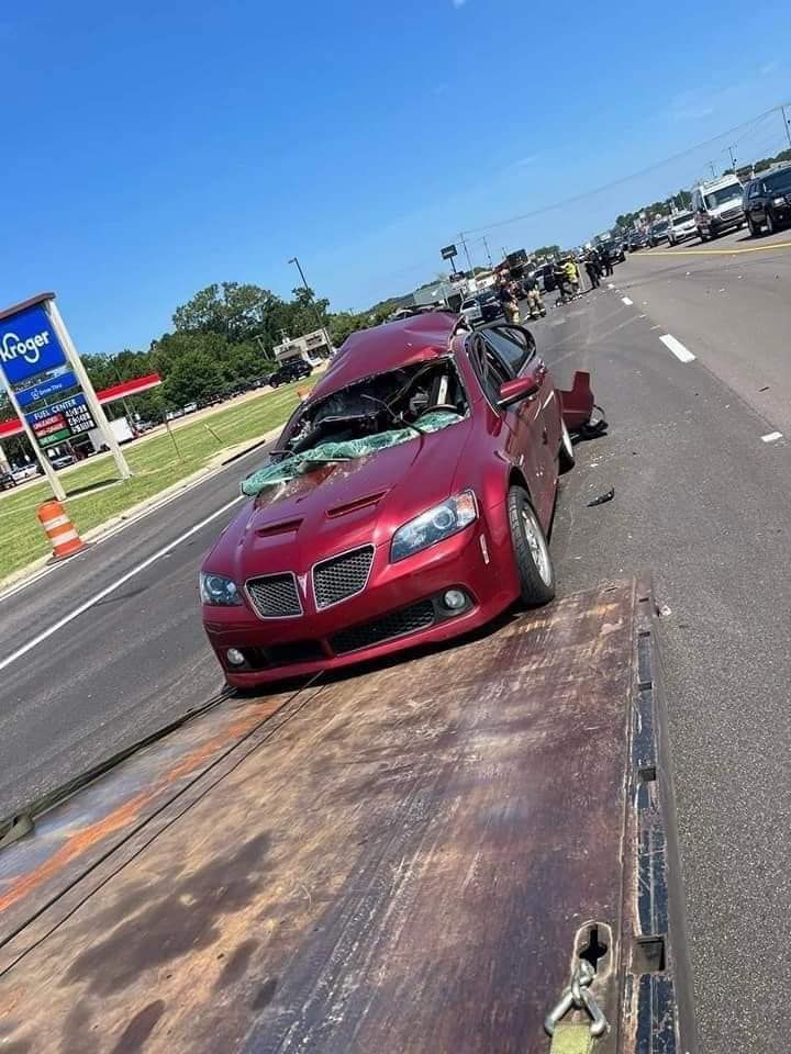 Red car with severe front-end damage on a tow truck.