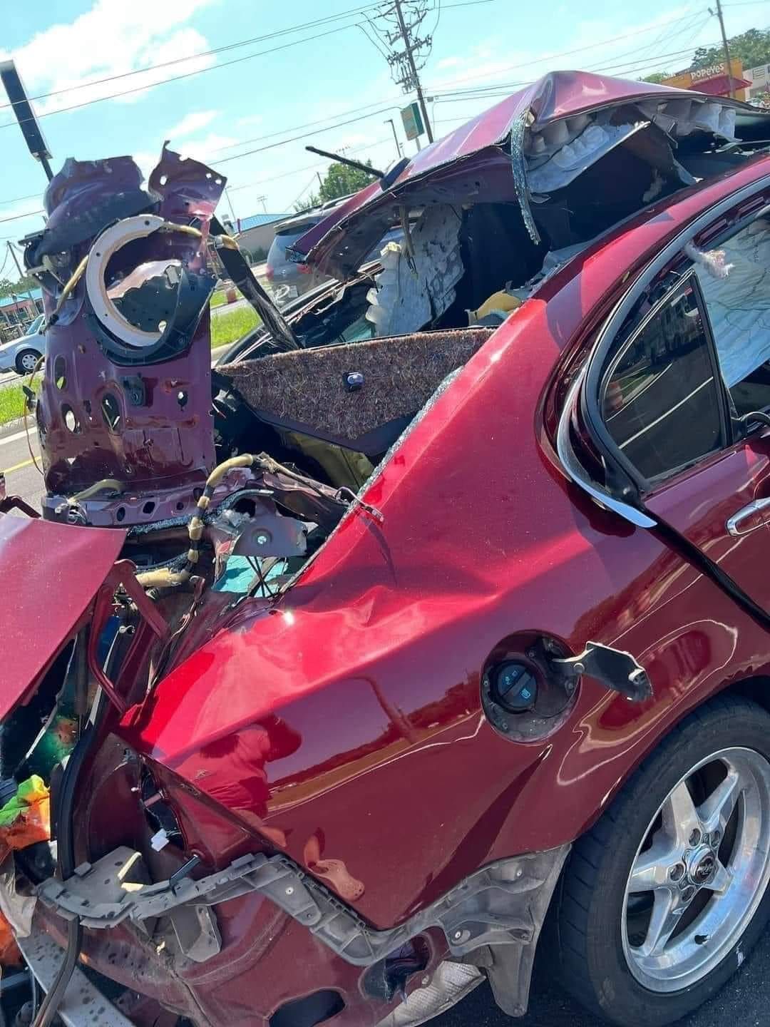 Damaged red car involved in a severe collision; roof crushed, extensive body damage.