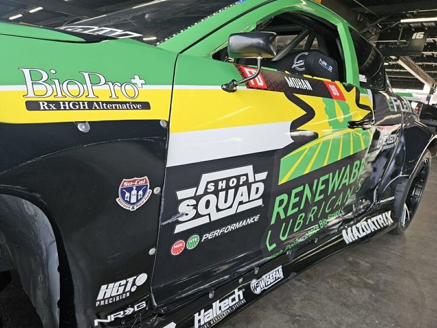 Green and black race car with sponsor logos, parked indoors.