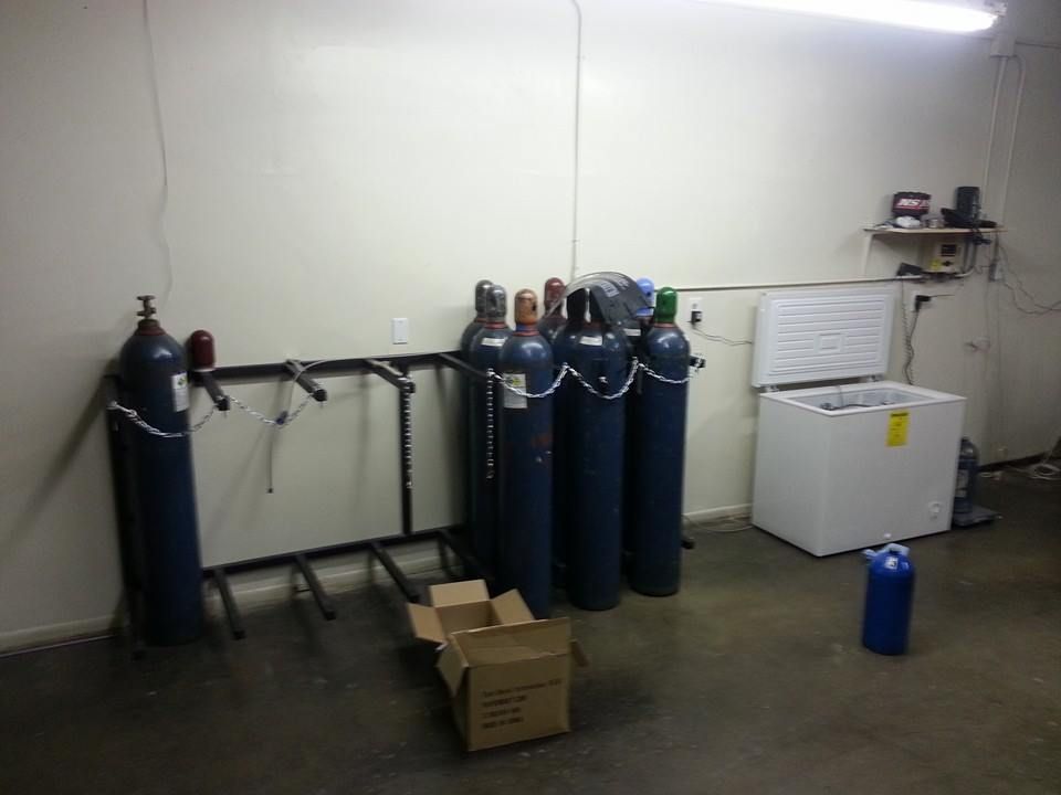 An industrial room with blue gas cylinders, a rack, open freezer, and cardboard box.