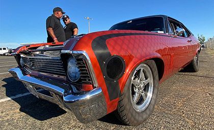 Classic orange muscle car with two men, on a paved surface.
