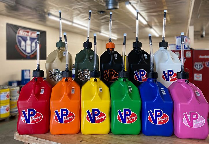Rows of VP Racing fuel jugs in various colors on a wooden surface, store interior.