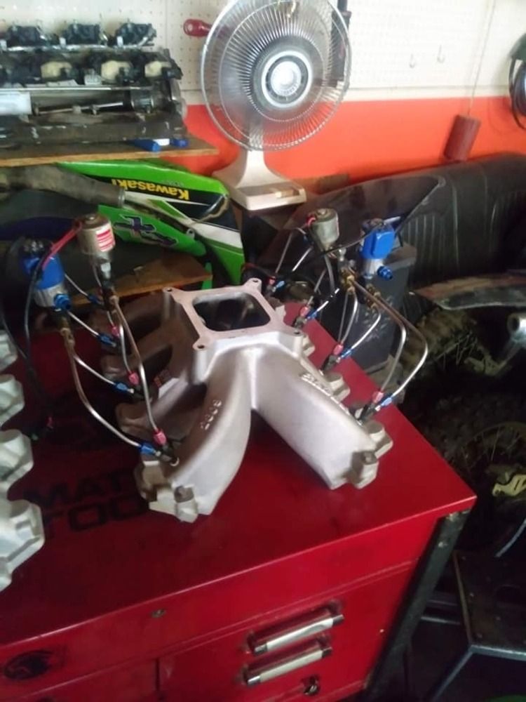 Gray intake manifold with blue fuel injectors on a red toolbox, workshop setting.
