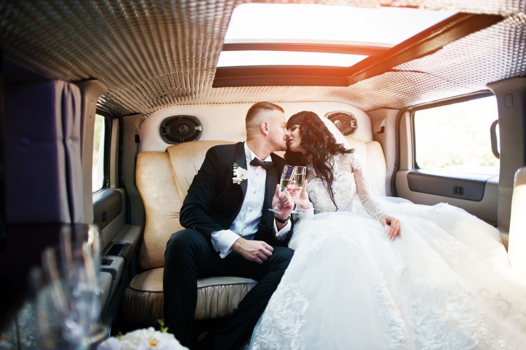 Bride and groom about to kiss inside a limo while holding a glass of champagne.