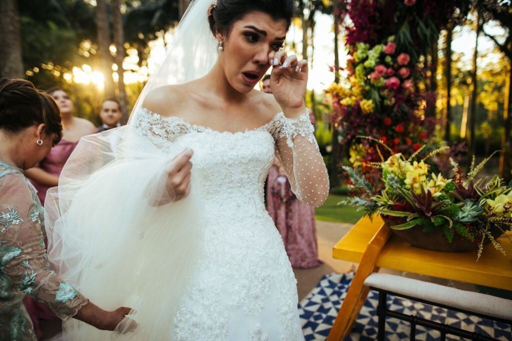 A bride is wiping away her tears as wedding guests stands on the background.
