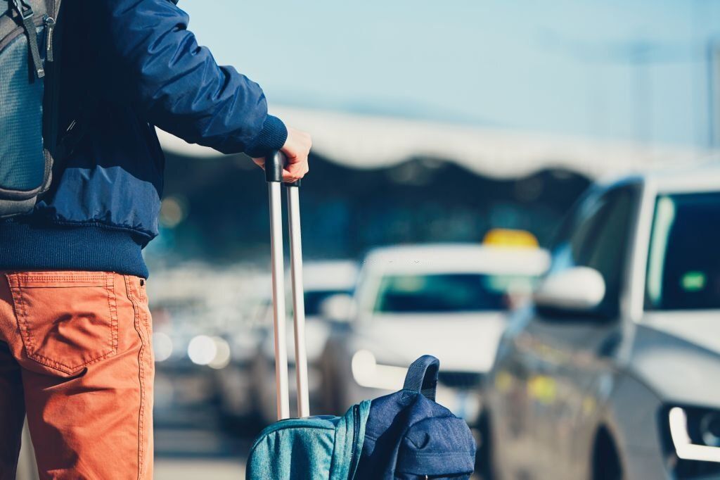 A man holds his luggage with a row of taxis in the background.