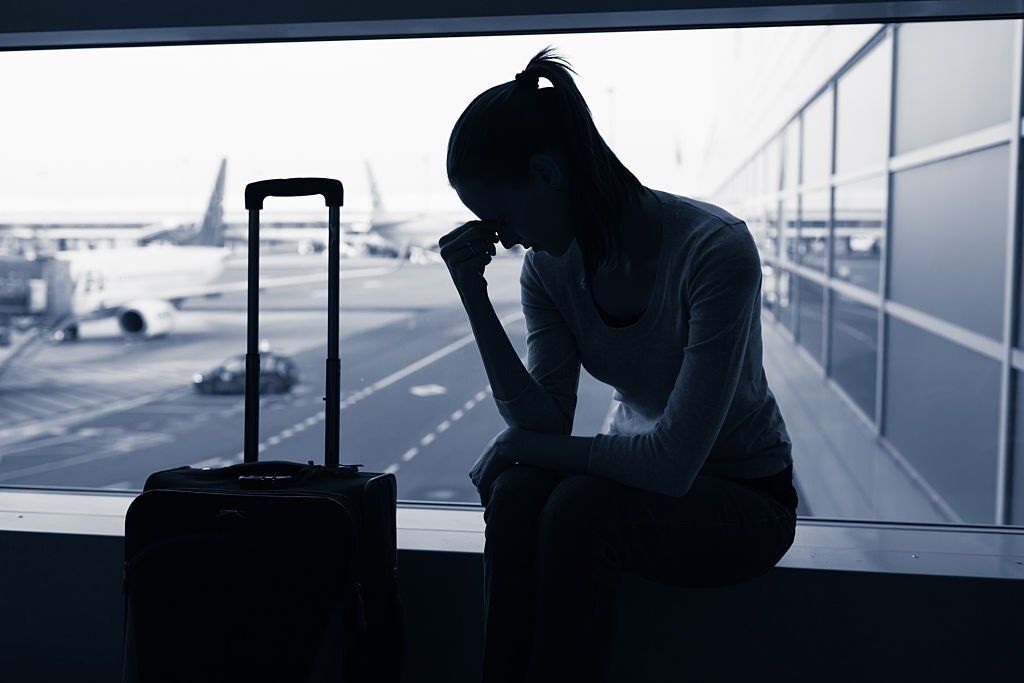 Silhouette of a stressed woman and her suitcase in airport.