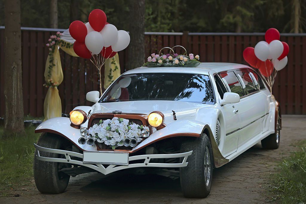 A white vintage wedding limousine decorated with flowers and white and red balloons