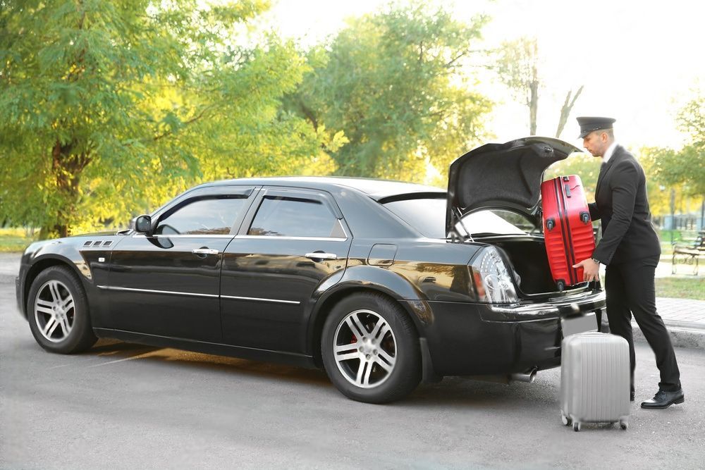 A chauffeur is putting a red luggage at the trunk of a luxury car.