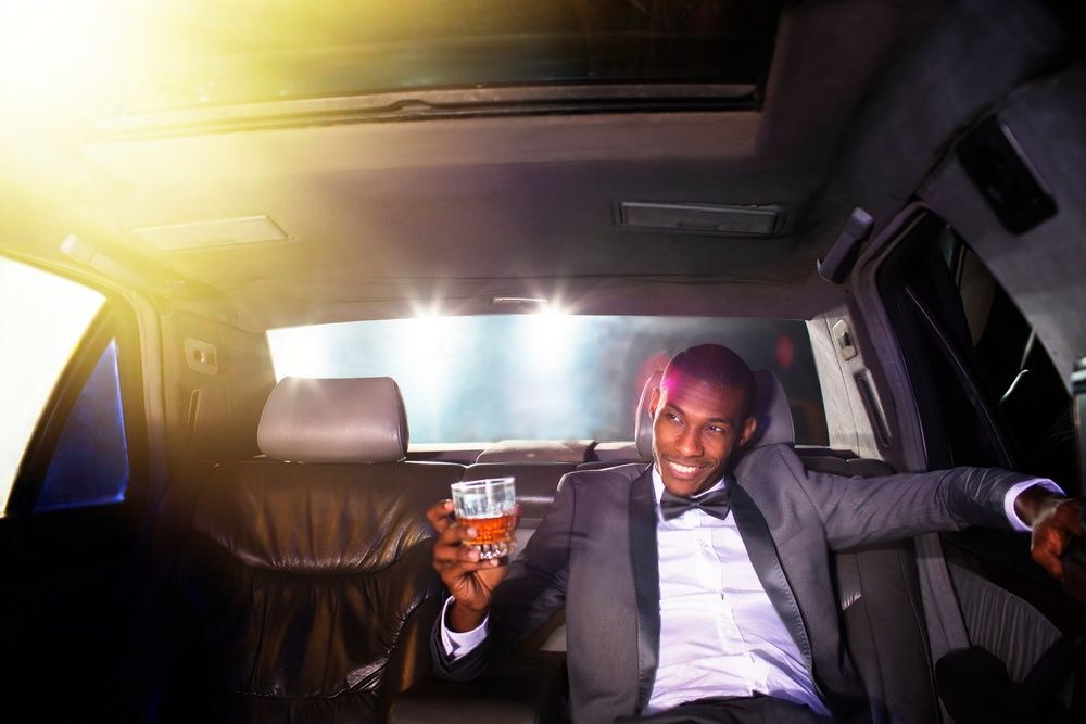Portrait of confident celebrity drinking cocktail inside limousine outside event.