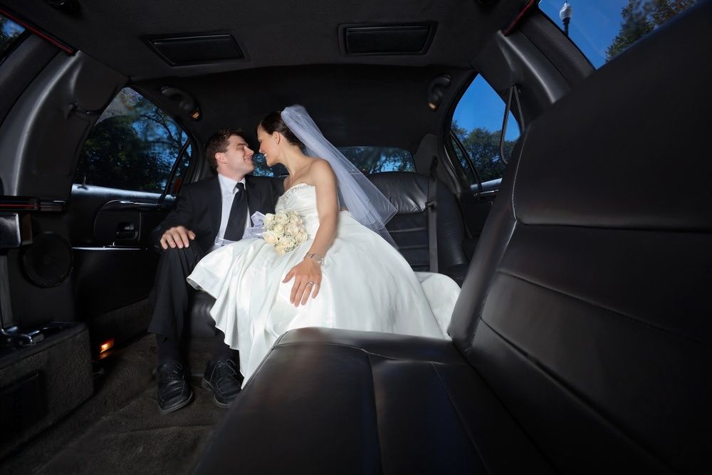 Bride and groom look at each other inside a limousine.