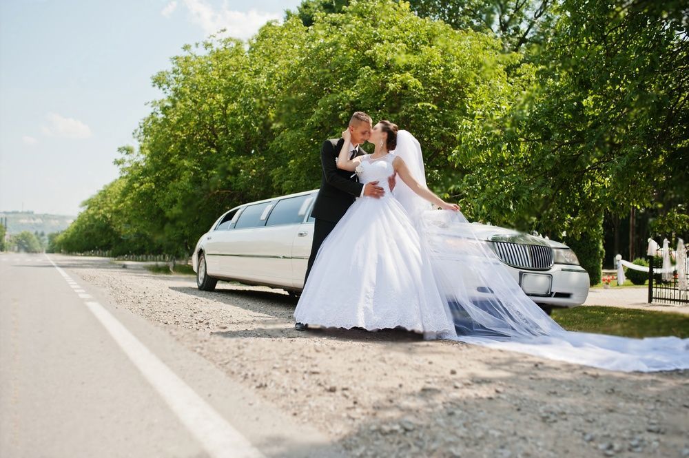 Happy groom and bride about stretch limousine in wedding day
