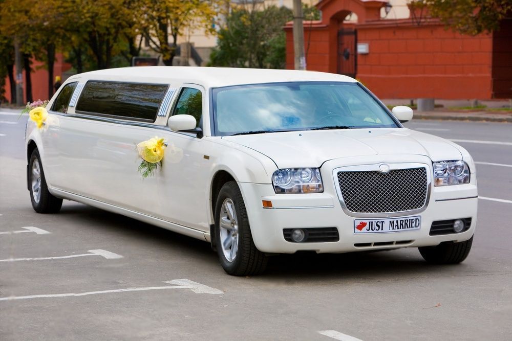 White wedding limo decorated with yellow bouquet of flowers  and a just married sign in front.