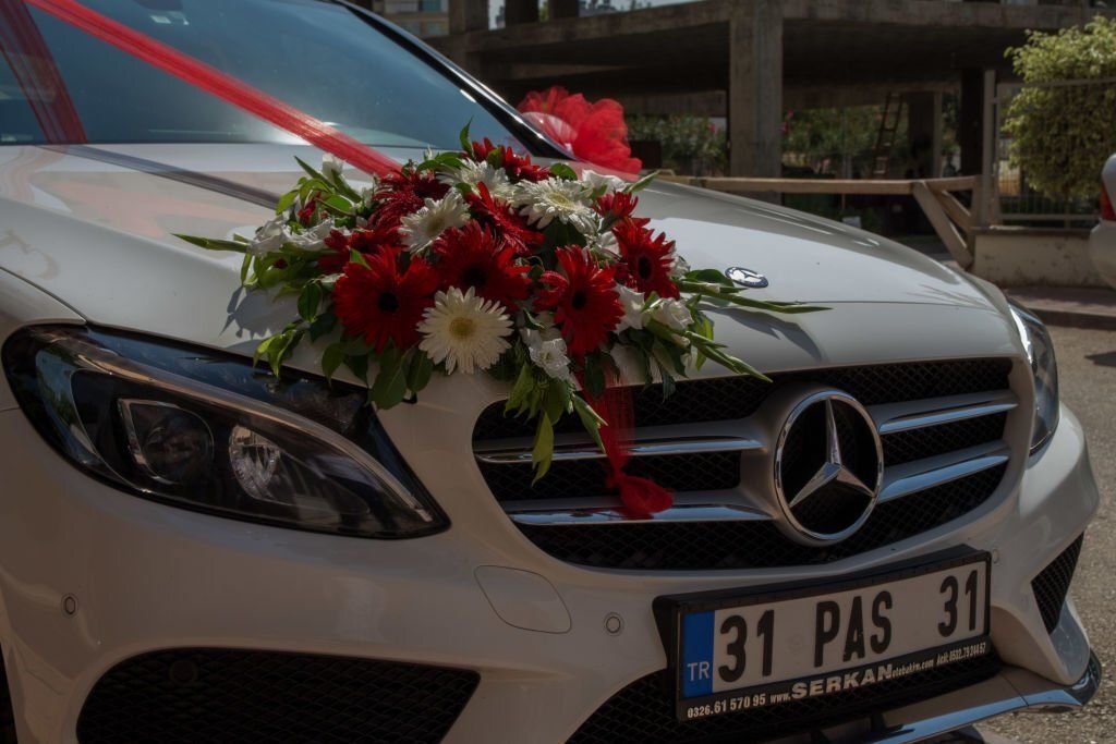 A Mercedes Benz car is decorated with flowers and red ribbon for a wedding.