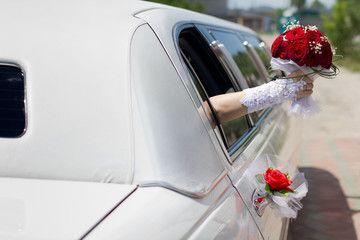 Bride waving from a limousine while holding a bouquet of red roses.