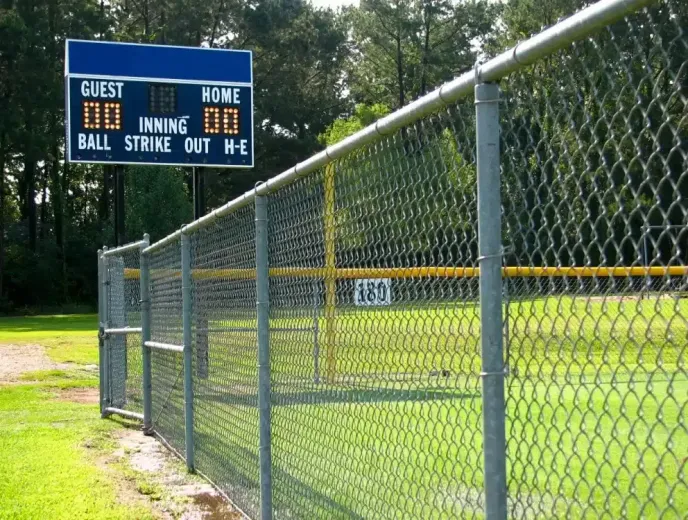 A baseball field with a chain-link fence and scoreboard. The scoreboard reads