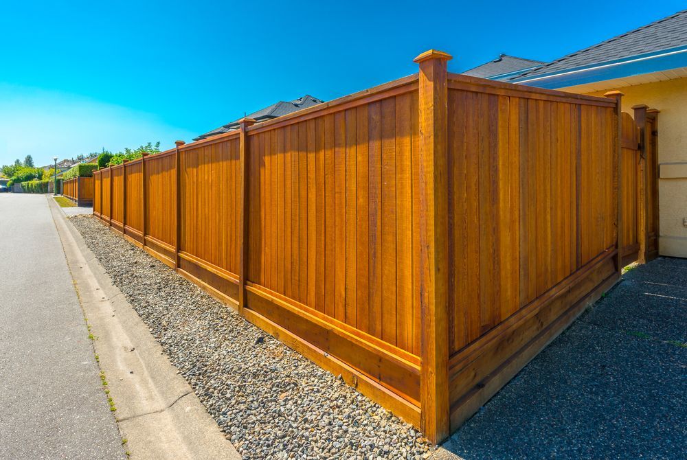 Wooden privacy fence along a road, stained brown and topped with decorative posts.