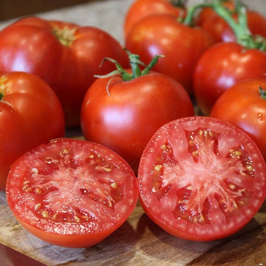 Fresh red tomatoes, with two sliced open on a wooden cutting board