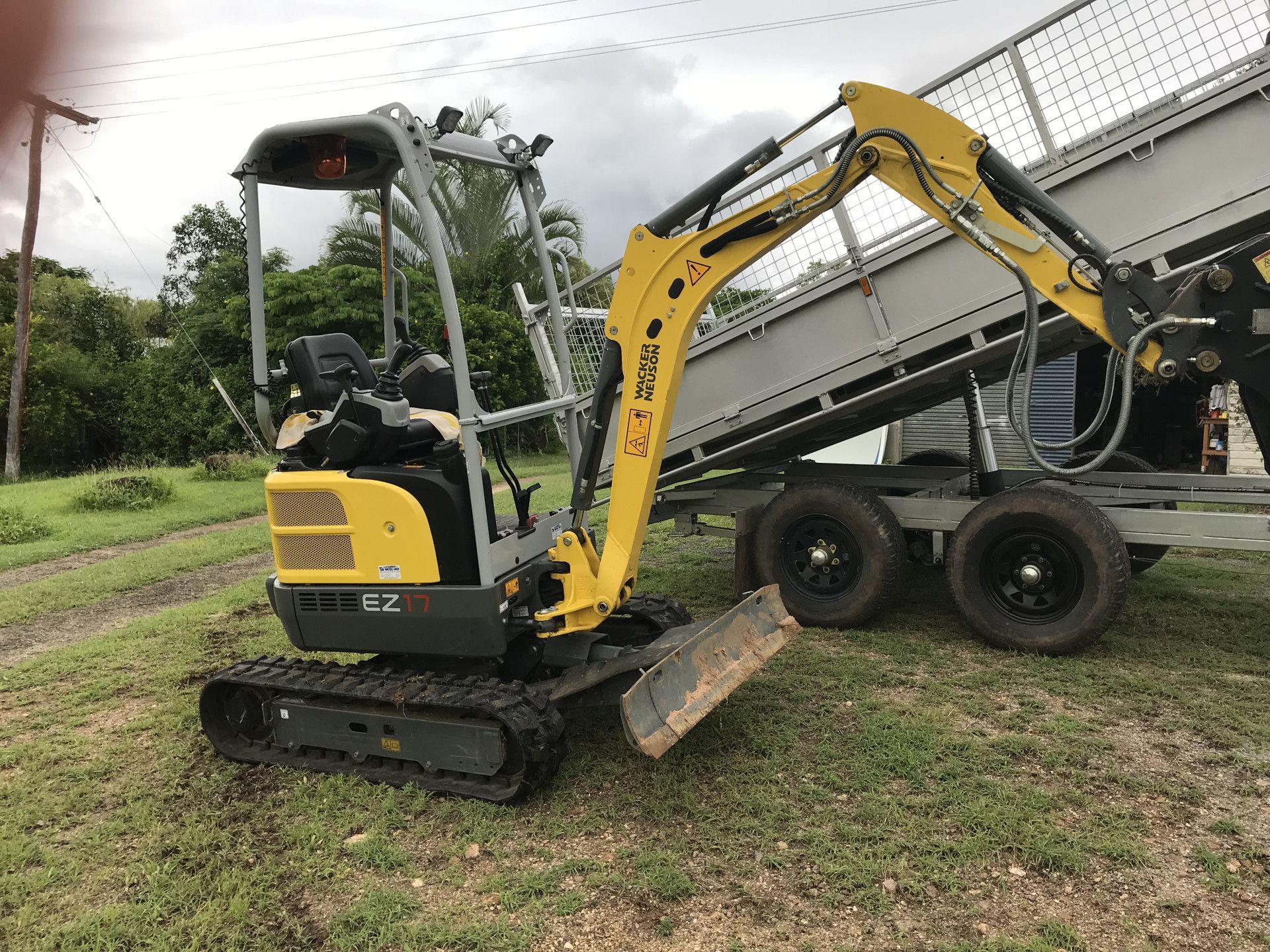 Yellow and black mini excavator next to a trailer on grass.— Mini Digger and Trailer Hire in Tablelands, QLD