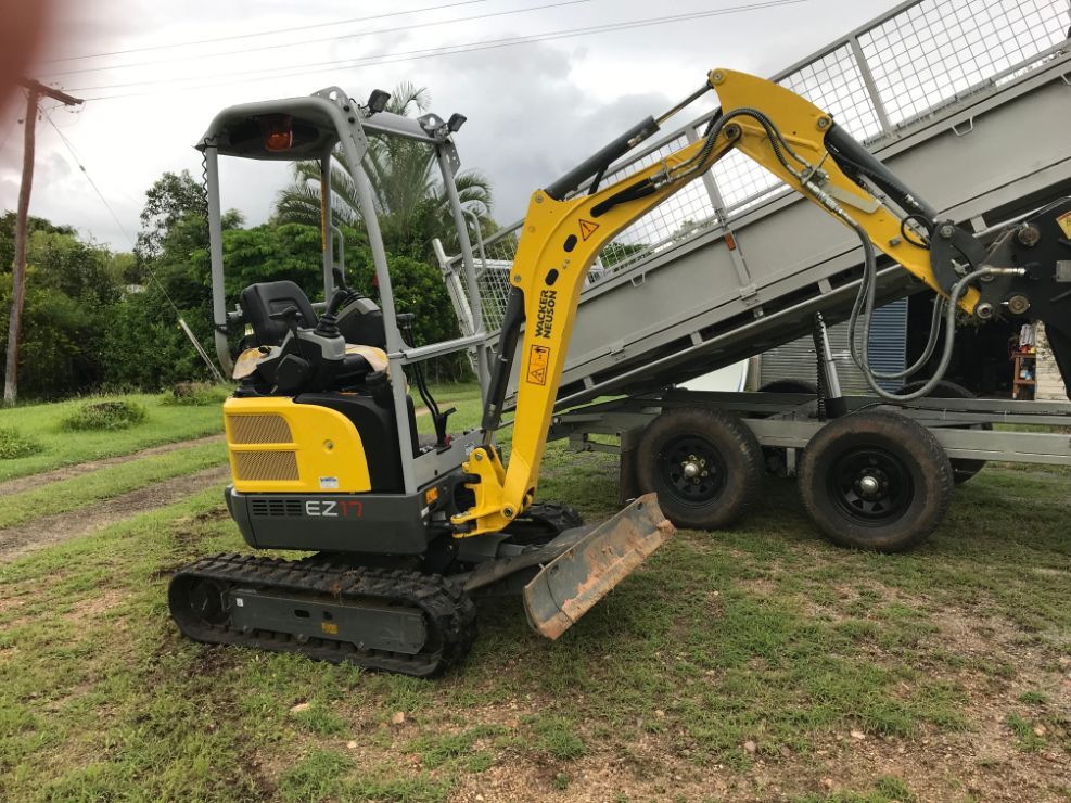 A Small Yellow Excavator is Parked Next to a Trailer — Mini Digger and Trailer Hire in Mareeba, QLD