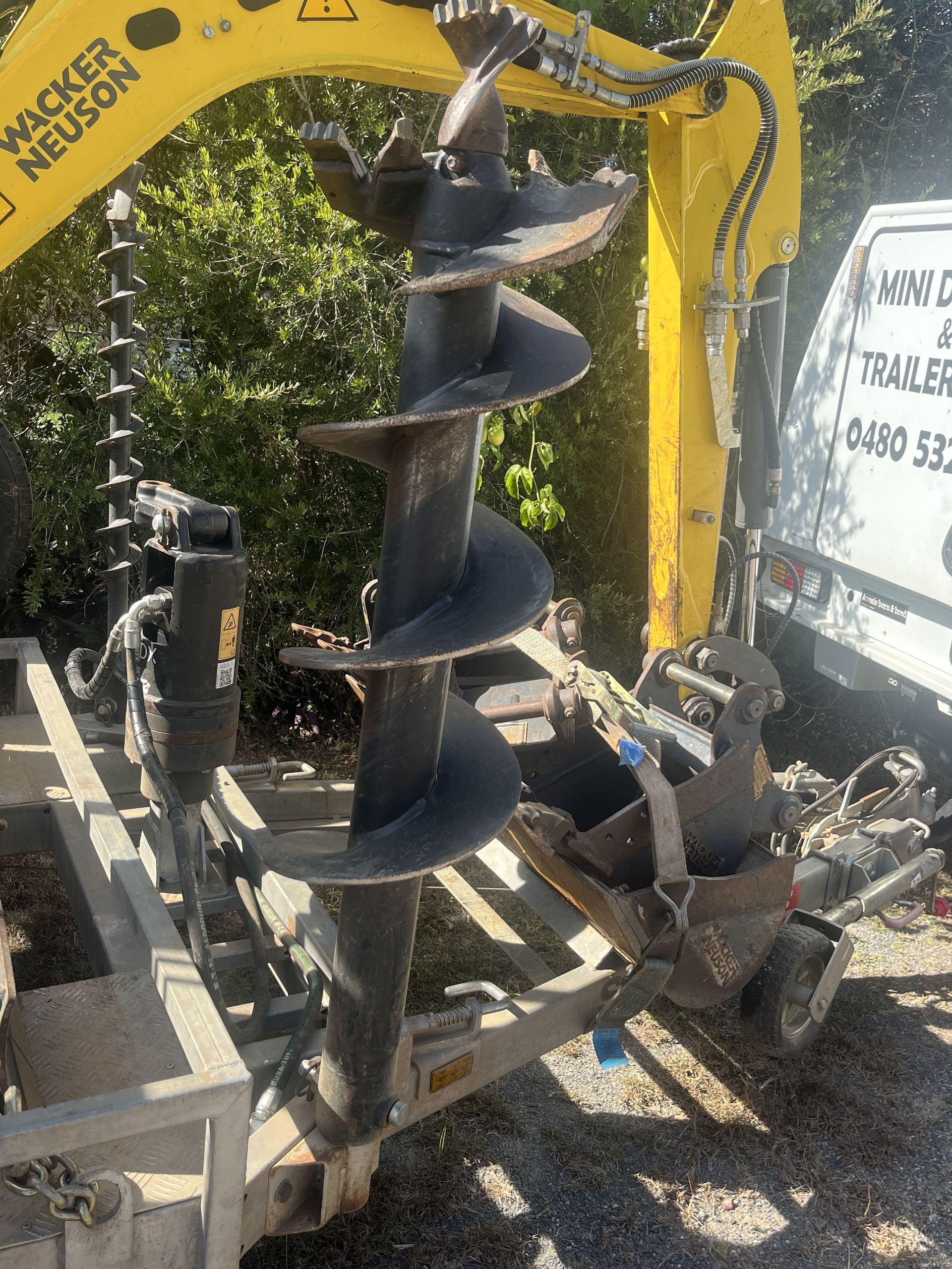 Yellow auger drill bit on a trailer, attached to a yellow excavator, ready to bore a hole.— Mini Digger and Trailer Hire in Mareeba, QLD
