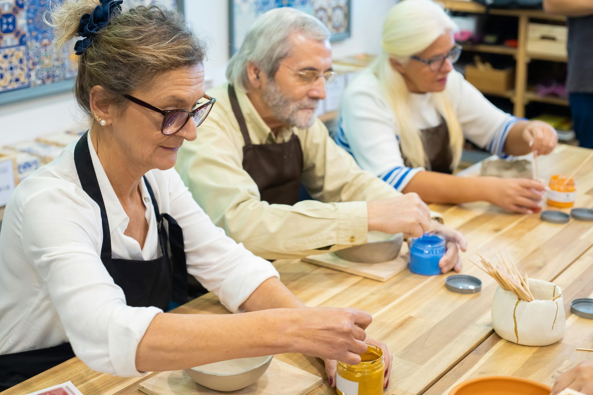 A group of older people are sitting at a table making pottery.