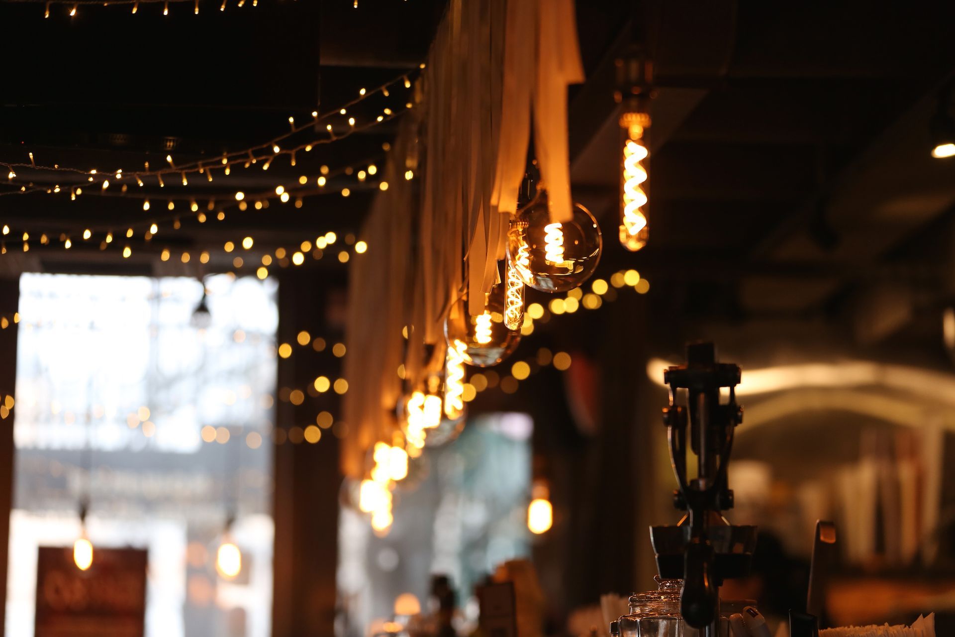 Warm Edison bulbs and string lights create a cozy, ambient glow in a restaurant setting. Warm Edison bulbs and string lights create a cozy, ambient glow in a restaurant setting.