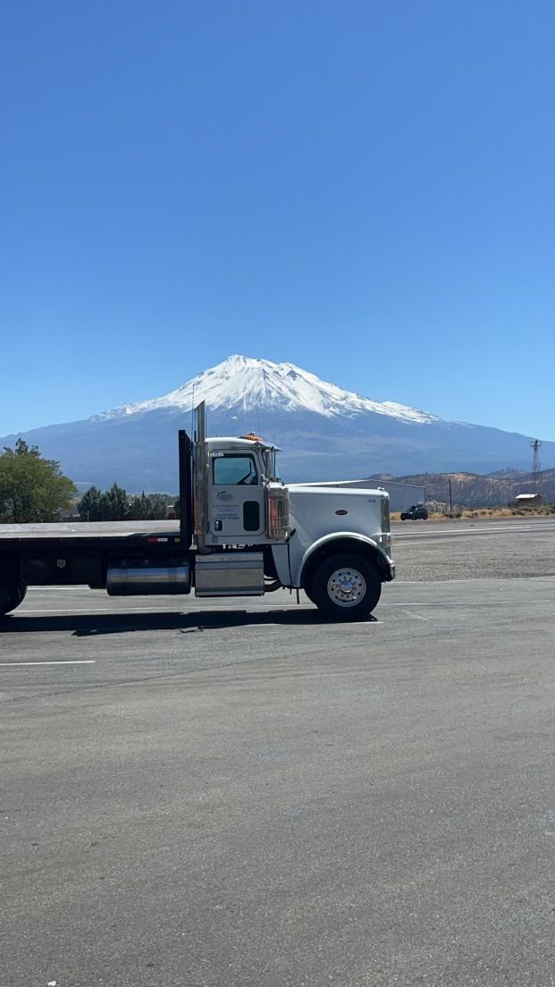 A flatbed truck is driving down a road with a mountain in the background.