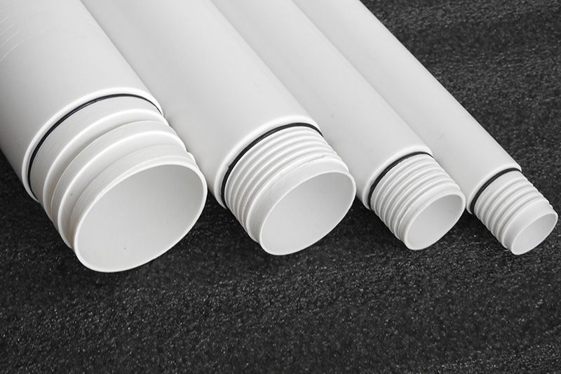 Four white plastic pipes are stacked on top of each other on a black surface.