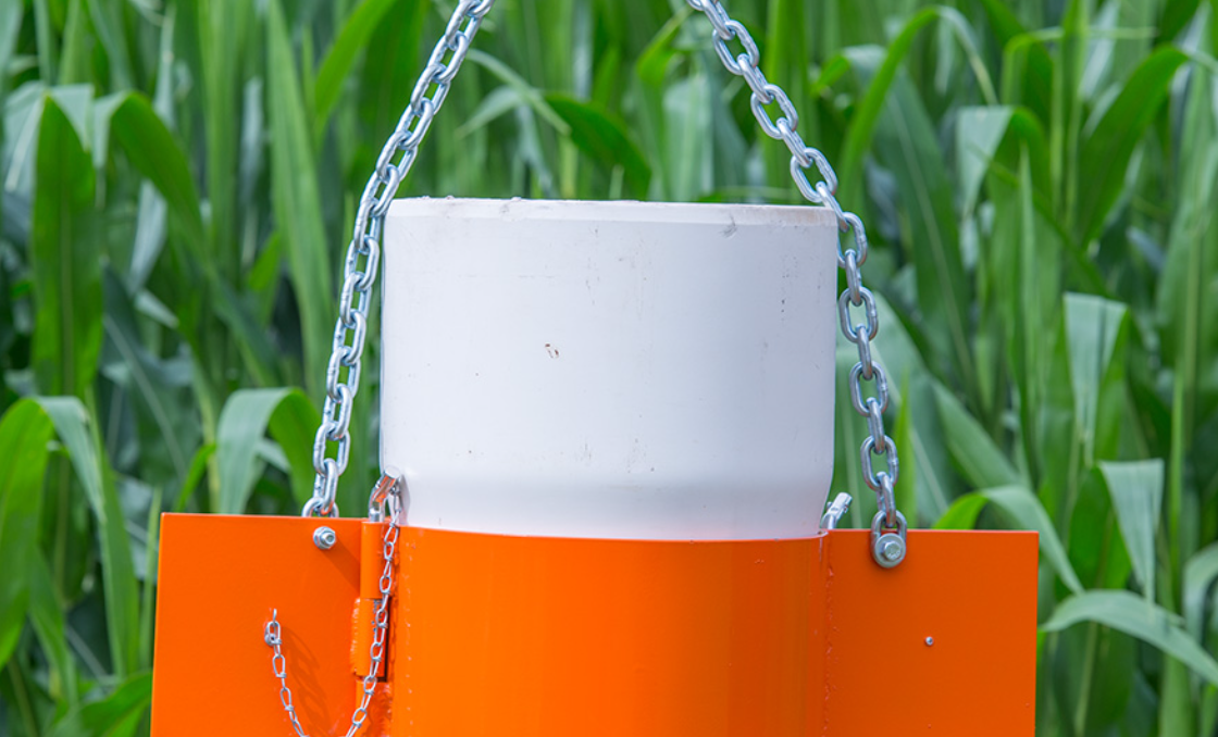 A white pipe is hanging from a chain in a field.