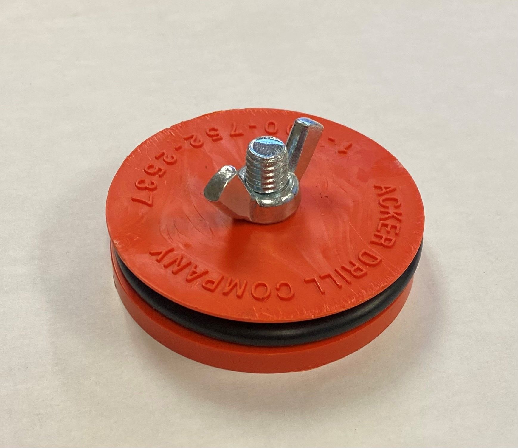 A red rubber cap with a screw on top that says acker drill company