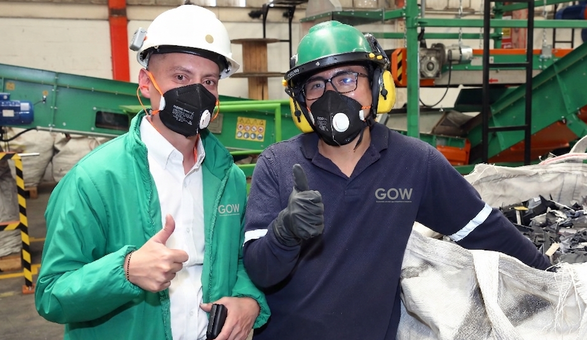 Dos trabajadores con cascos y mascarillas posan dentro de una instalación industrial, haciendo el gesto de aprobación con el pulgar.