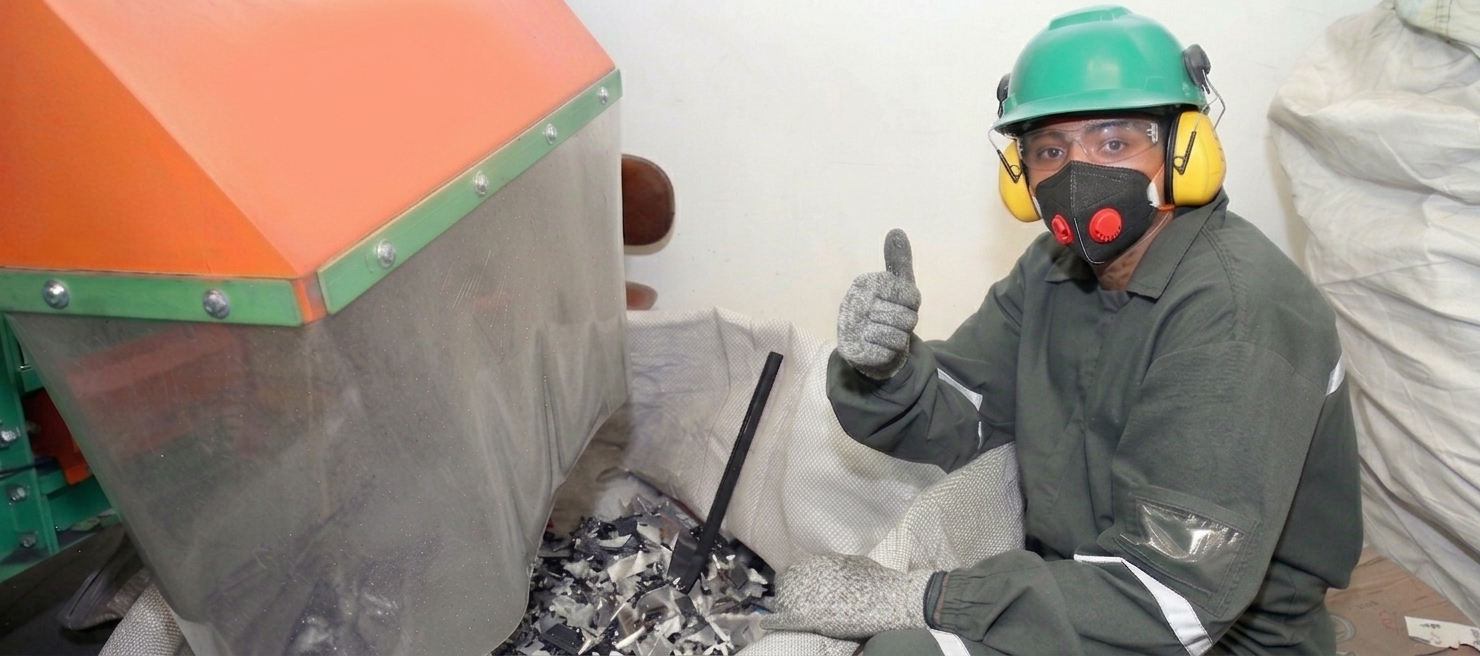 Un trabajador con casco y respirador levanta el pulgar junto a una gran máquina industrial y escombros.