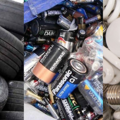Montón de baterías usadas mezcladas con neumáticos de coche y tubos blancos enrollados en un contenedor de reciclaje.