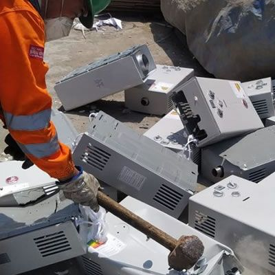 Un trabajador con equipo de seguridad naranja manipula escombros entre cajas electrónicas blancas rotas en un vertedero.
