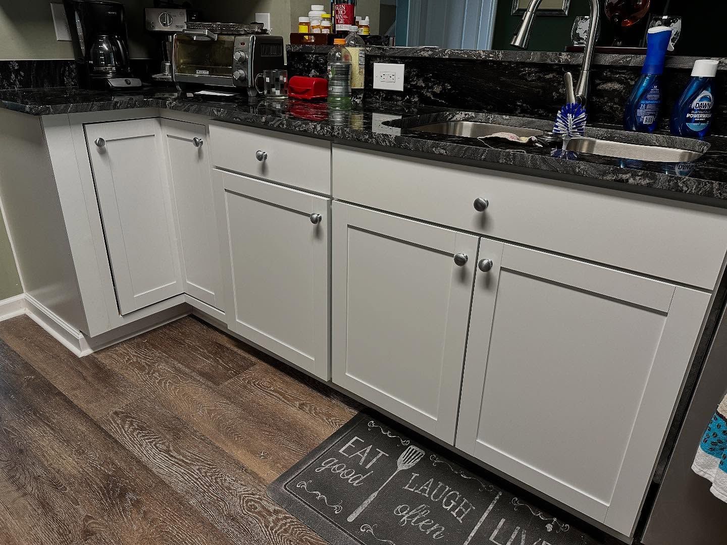 Kitchen sink area with white cabinets, dark granite countertop, and wood-look floor.