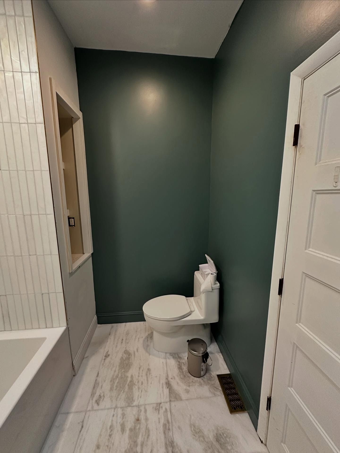Small bathroom with dark green walls, white tile, and a toilet beside a doorway.