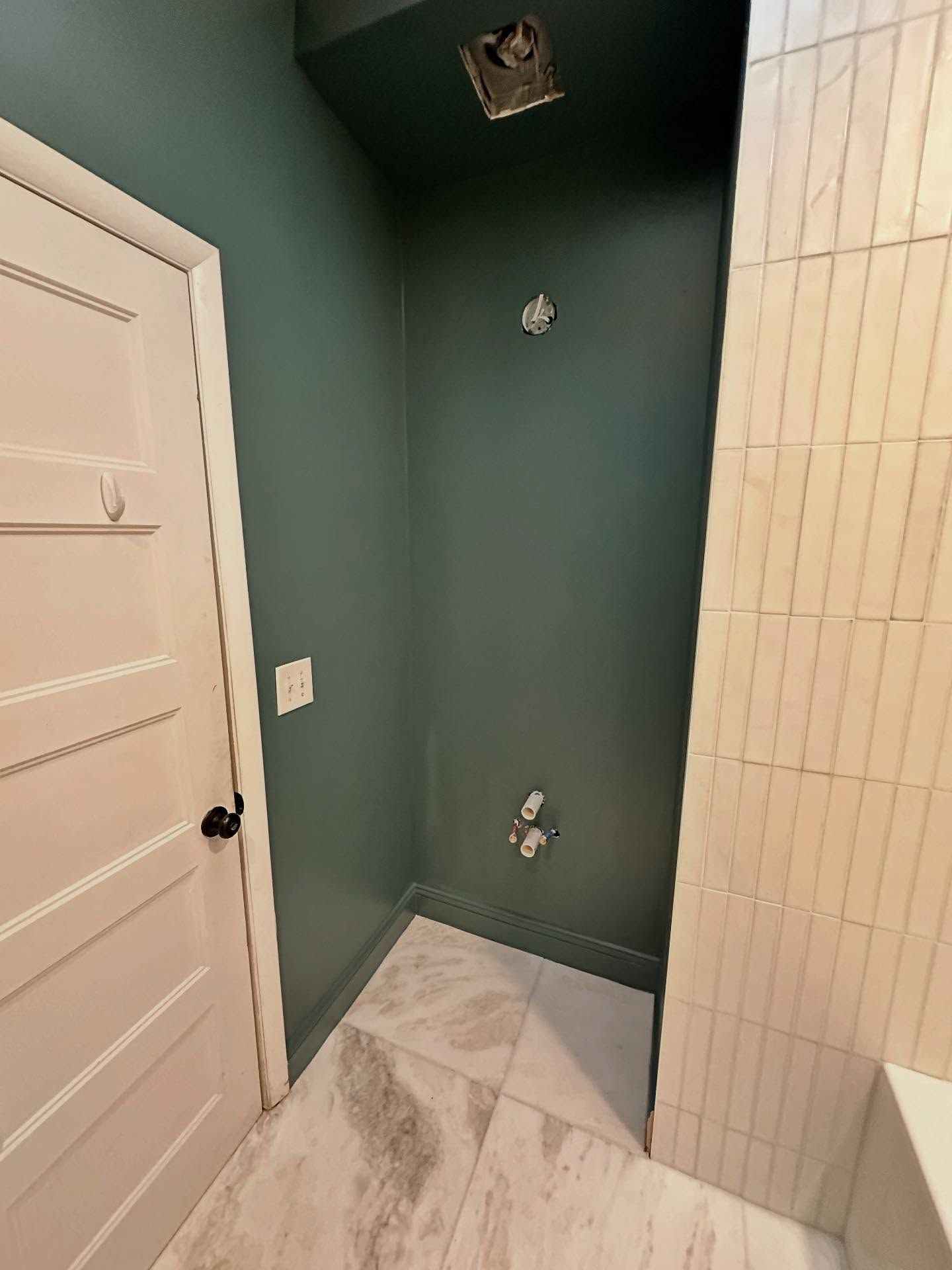 Small bathroom corner with green walls, white tile floor, and a shower hookup next to a door.