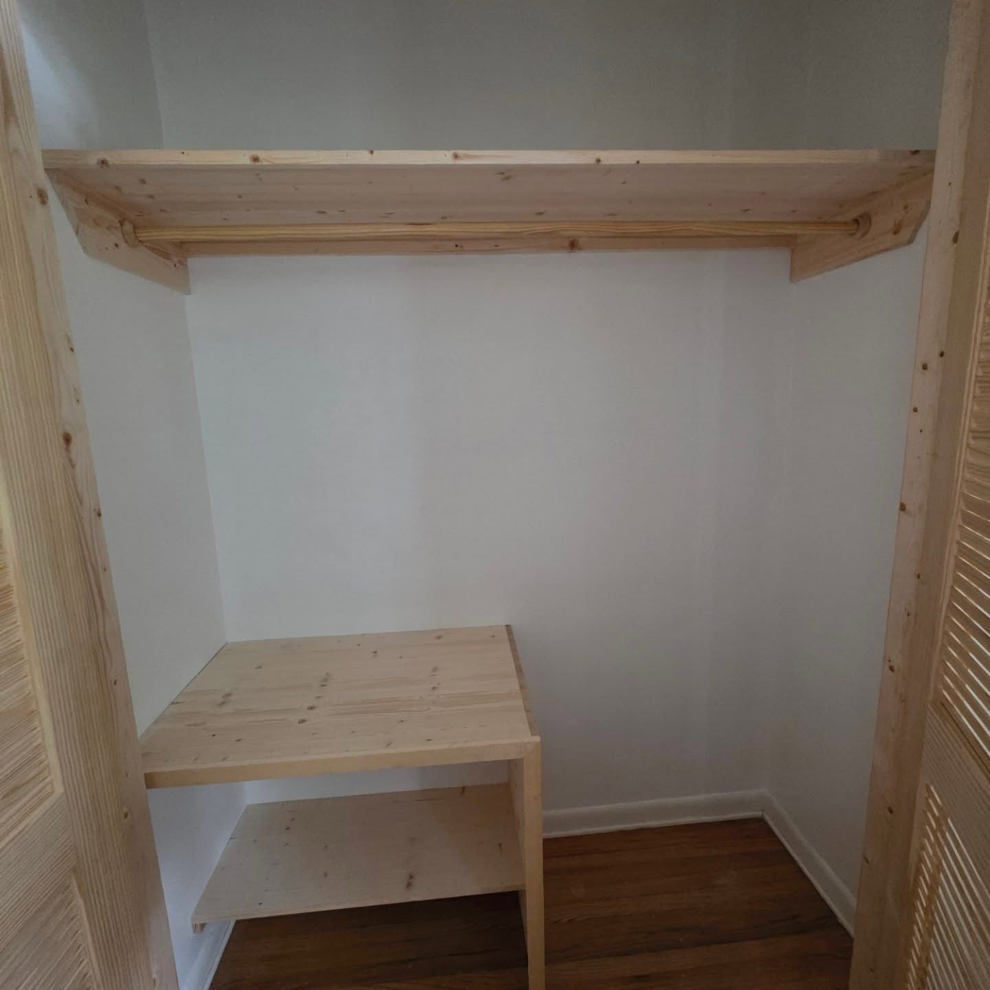 Small empty closet with a wooden shelf and a lower wooden storage unit on hardwood floors.