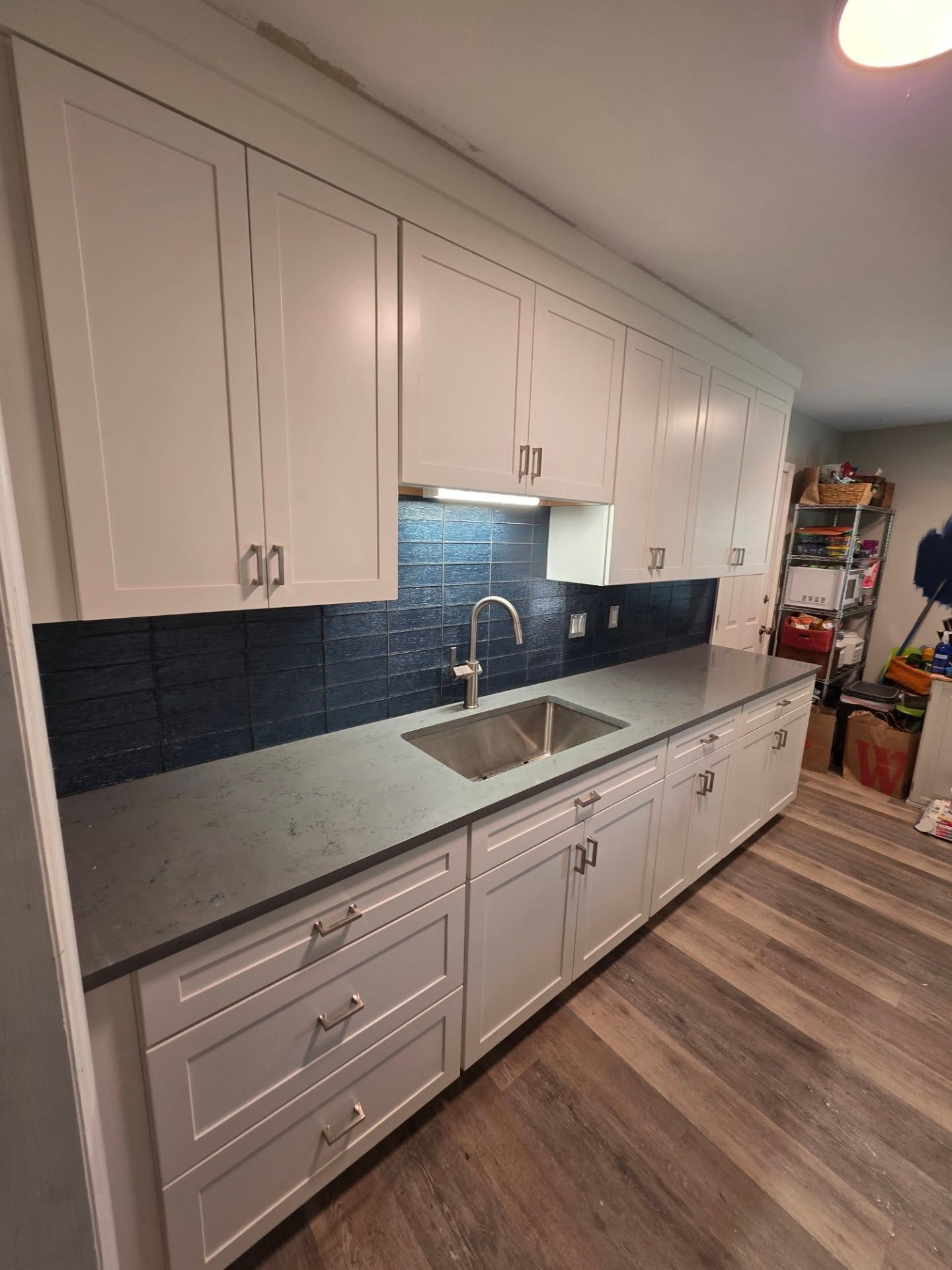 Modern kitchen with white cabinets, gray countertops, dark backsplash, and wood-look flooring