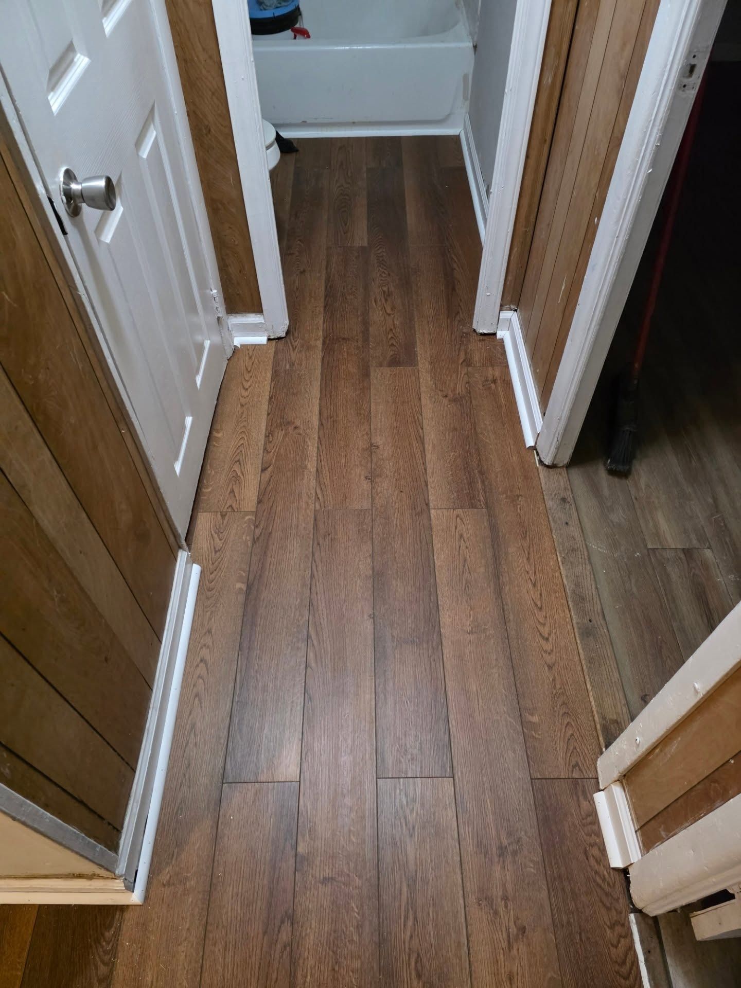 Wood-look hallway floor with white trim and doorways on both sides