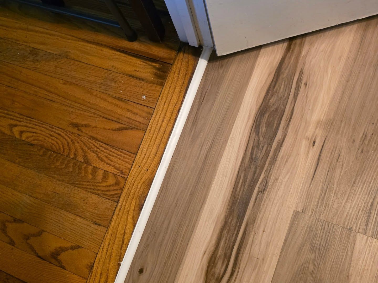 Wood and vinyl flooring meet at a doorway with a white transition strip.