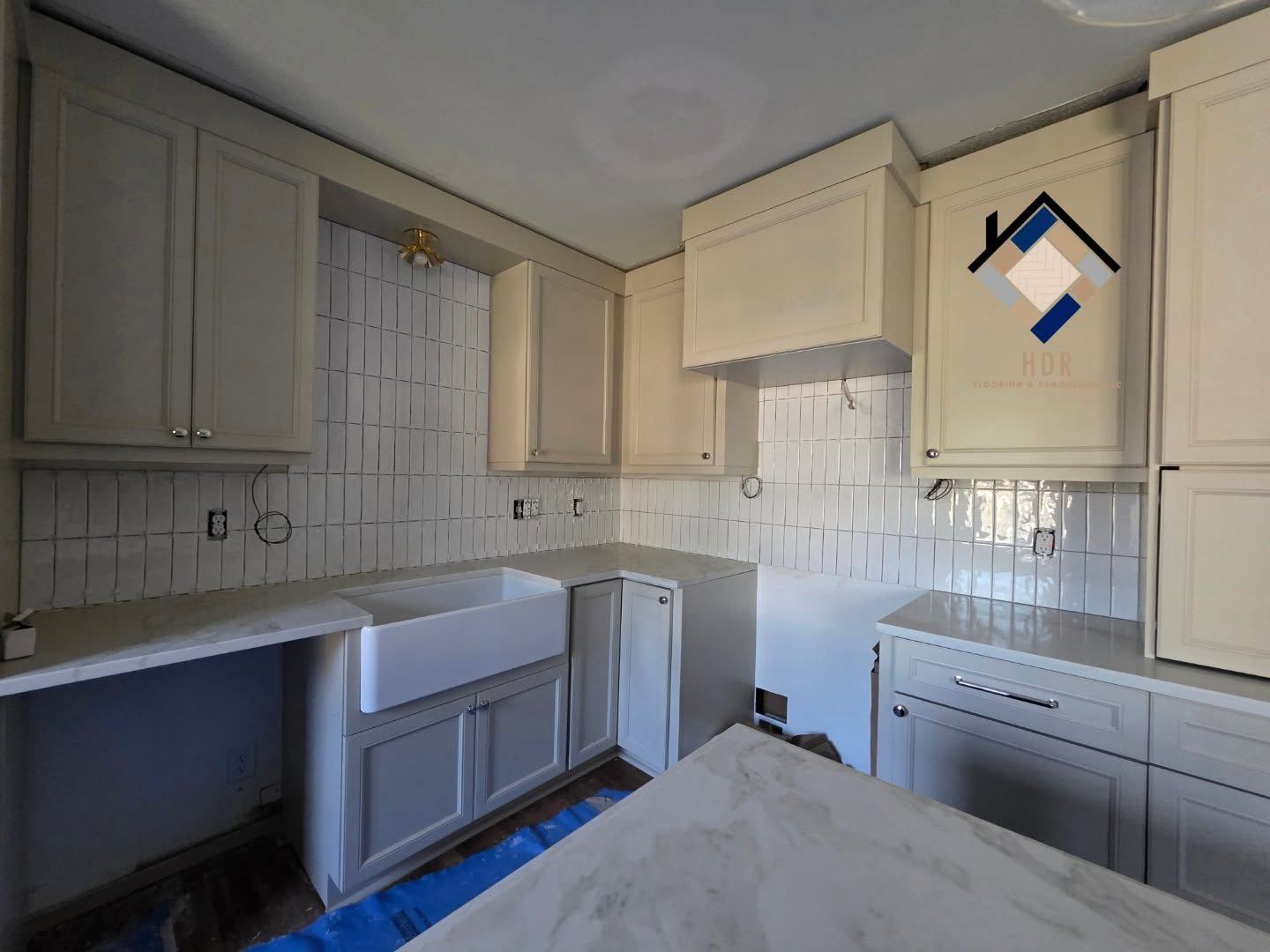 Small white kitchen with cabinets, tiled backsplash, sink, and countertop, with a white stove and hood.