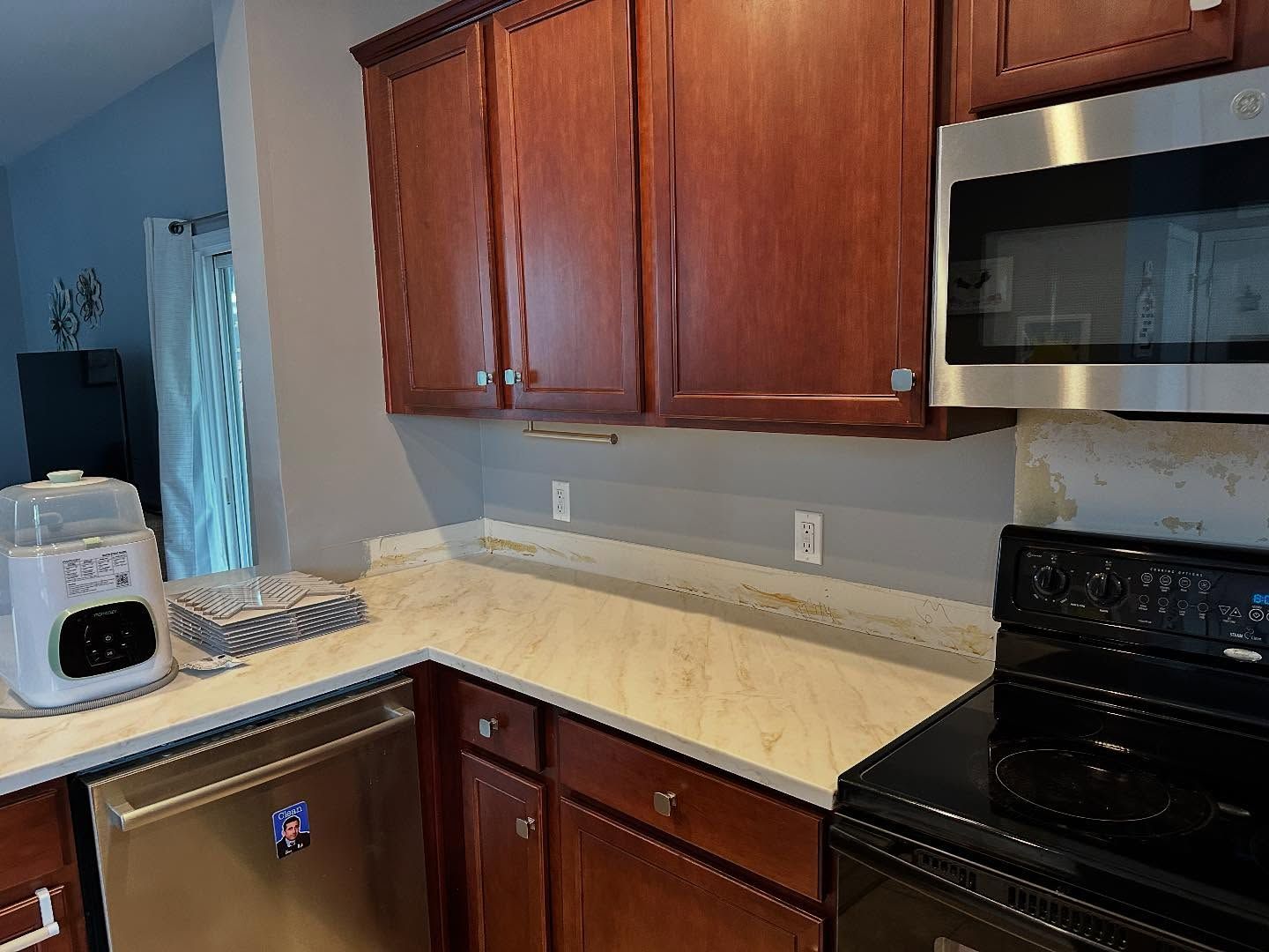 Kitchen corner with wooden cabinets, white countertop, black stove, and microwave above.