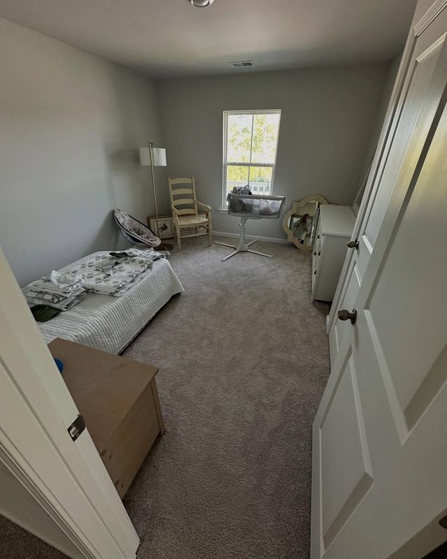 Small bedroom with unmade bed, chairs by a window, dresser, and white walls.