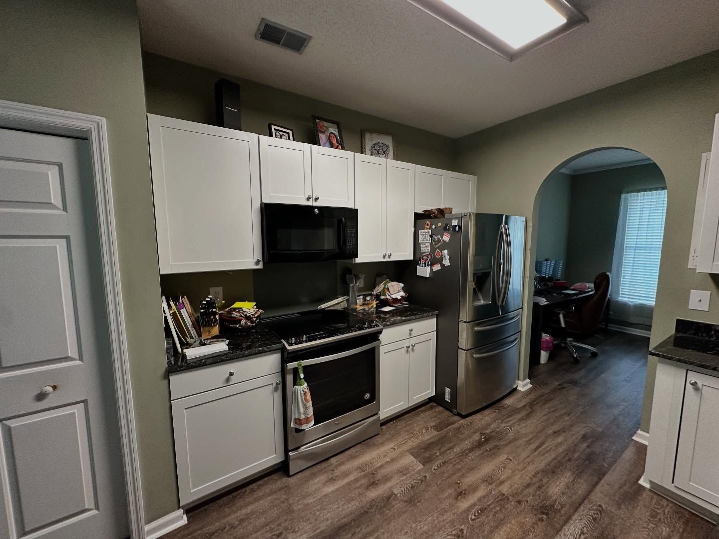 Modern kitchen with white cabinets, black appliances, and a stainless steel fridge, opening to a living area.