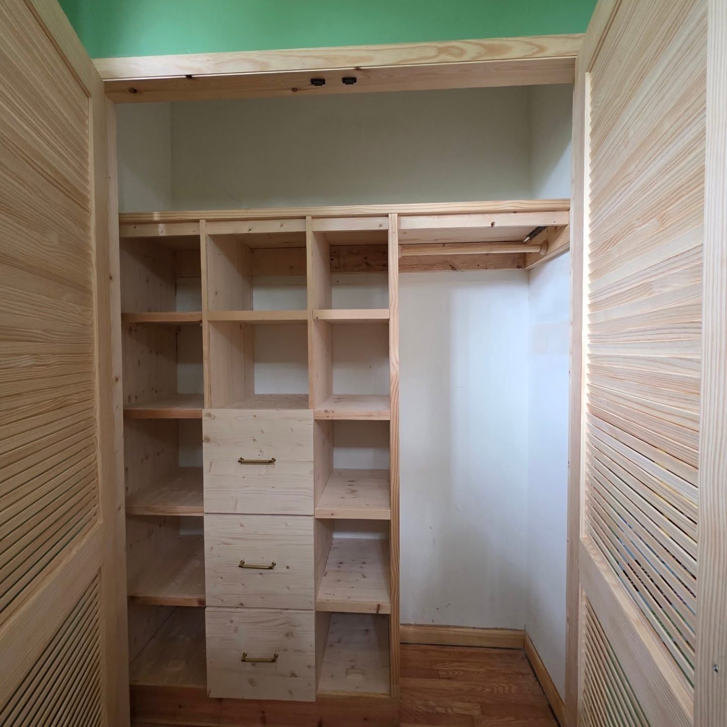 Empty walk-in closet with built-in wooden shelves, drawers, and hanging space, viewed through open doors.