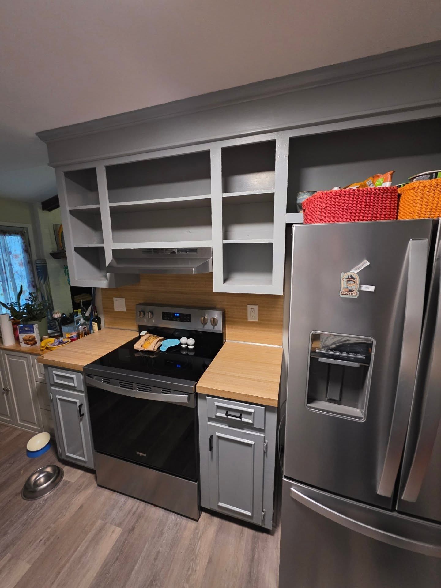 Kitchen with open gray cabinets, wood countertops, black stove, and stainless steel refrigerator