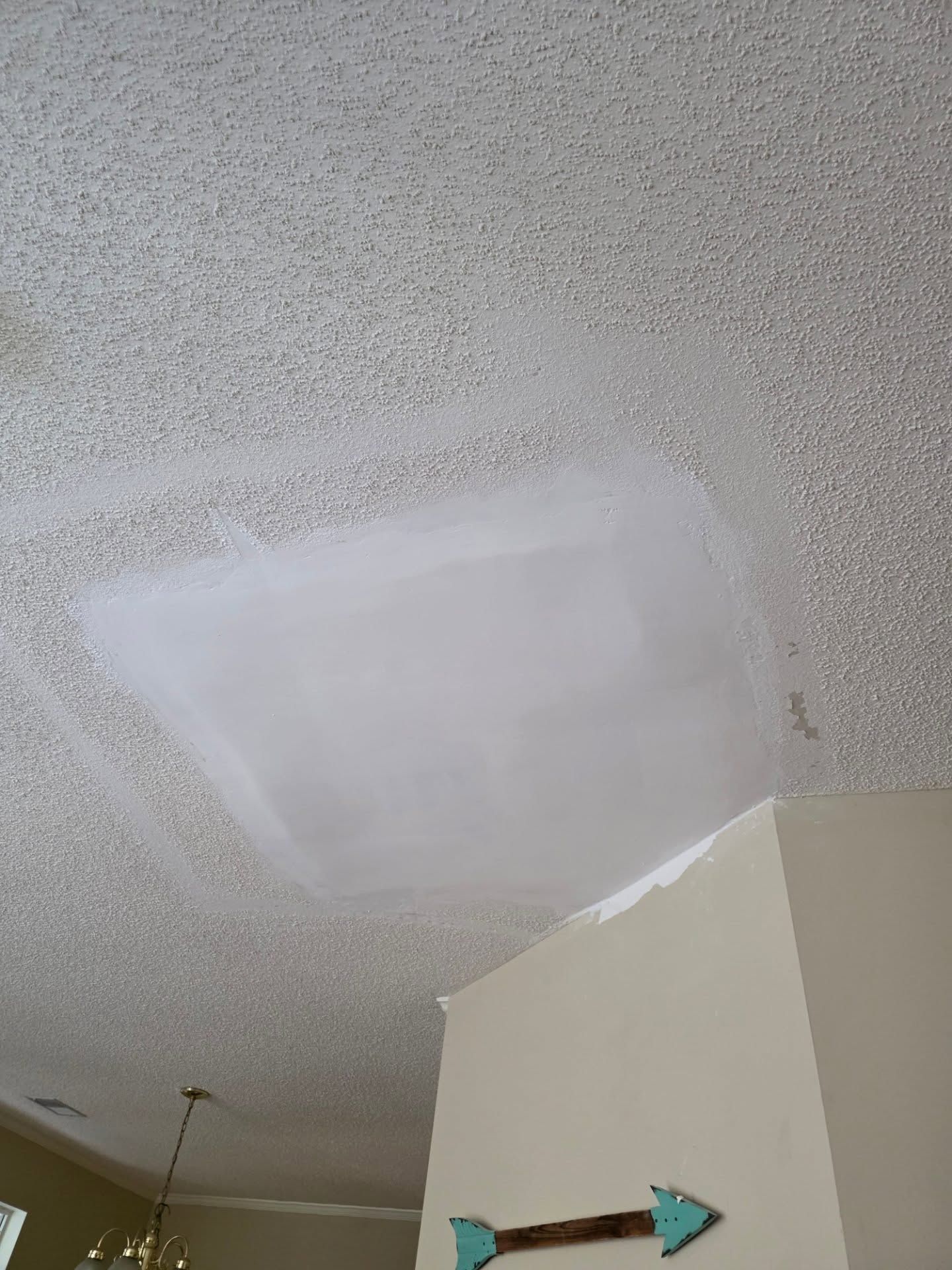 Ceiling with a large patched white area near a wall and hanging light fixture