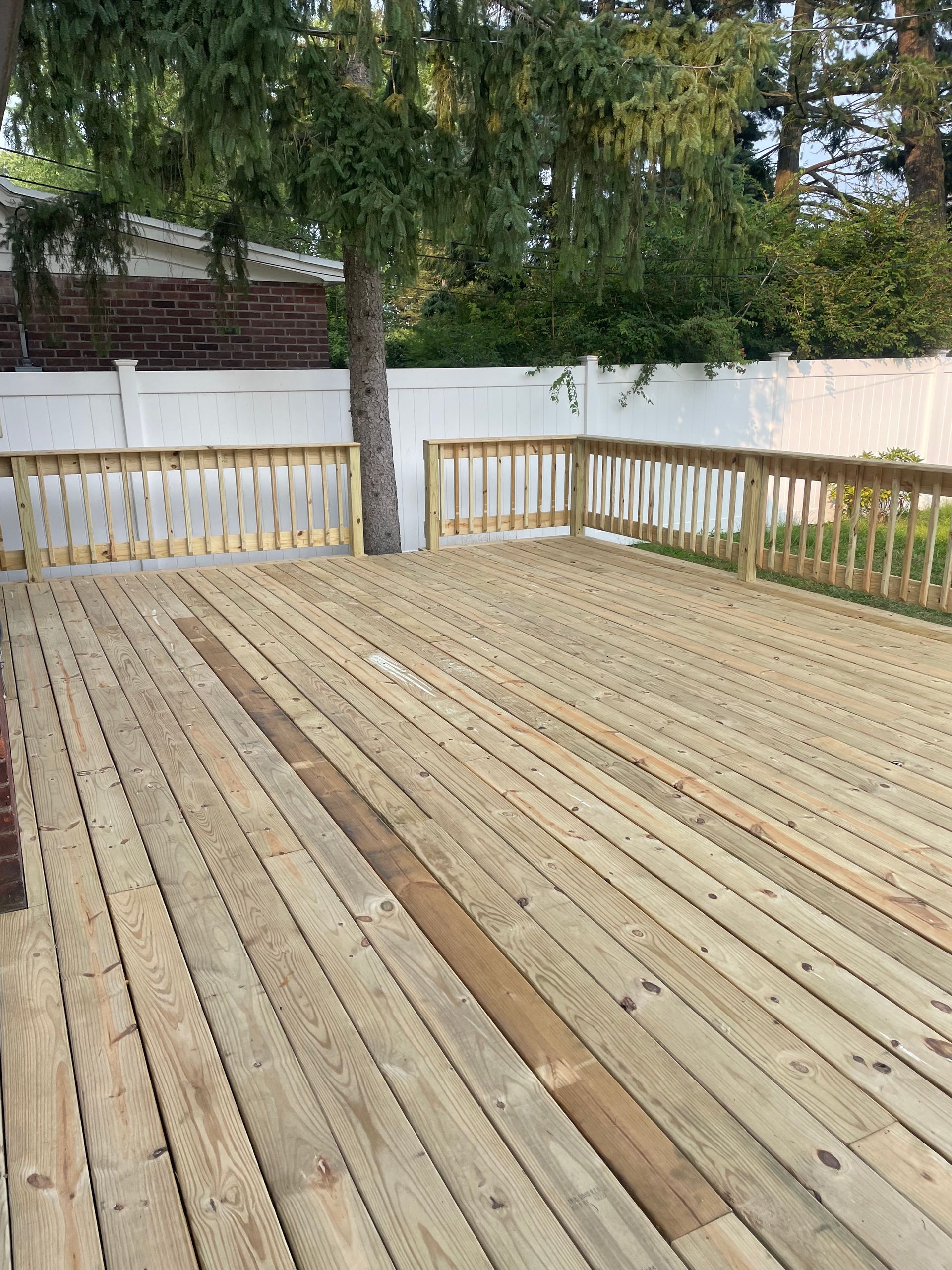 An empty wooden deck with a white fence and trees in the background.